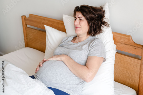Photography Pregnant woman in discomfort lying on a bed, holding her belly.