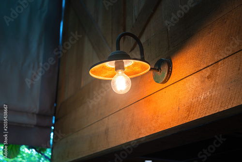 Fotografía A classic style lighting sconce with glowing in warnlight shade that installed on wooden wall at the barn house