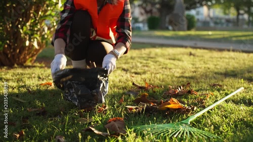 Female municipal park worker cleaning fallen leaves and collecting waste in city park, supporting environmental protection and urban green space maintenance.