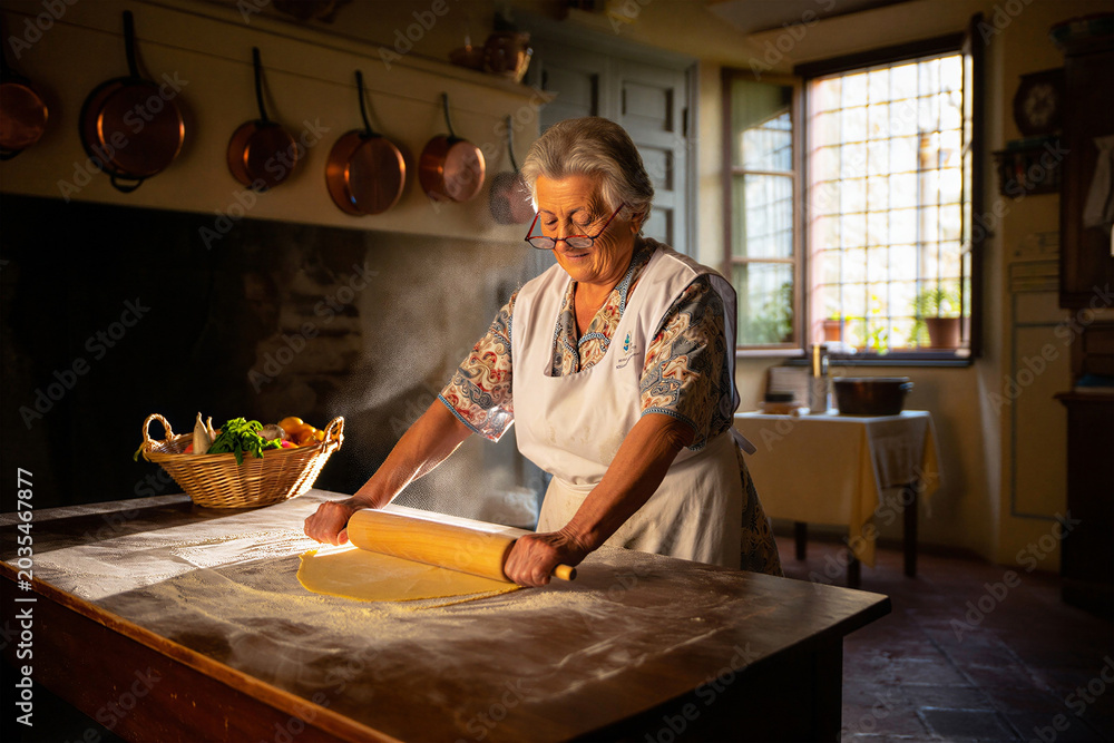 Fototapeta premium Elderly woman rolling out fresh pasta dough in a rustic kitchen