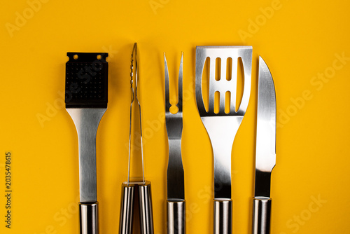 Cuadro en lienzo Collection of kitchen grilling utensils laid out on a vibrant yellow background,
