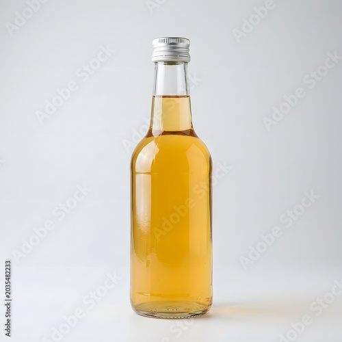 Clear glass bottle filled with golden liquid, likely apple cider or juice, against a plain background