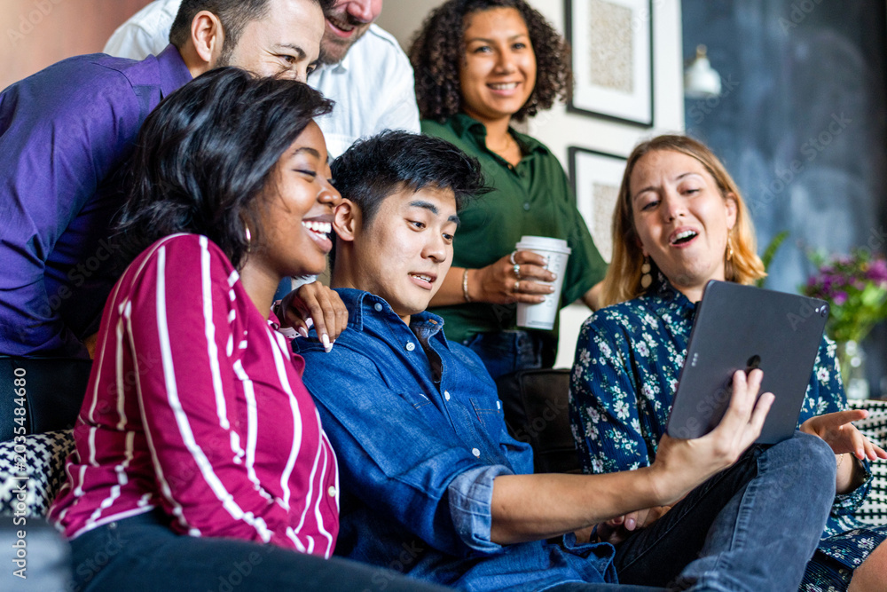 Fototapeta premium Group of diverse people smiling and looking at a tablet together.