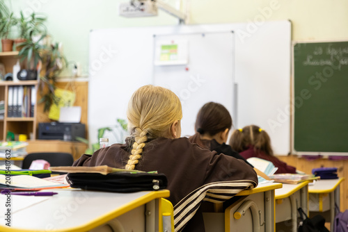 A primary school child sits at a desk listening to their teacher during a classroom lesson to illustrate academic education, effective study habits, and focused student development