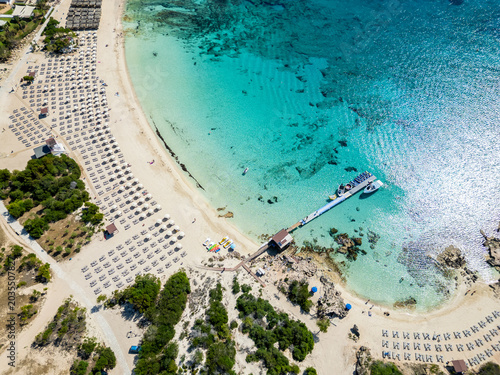 Aerial shot of a Makronissos beach in Ayia Napa, Cyprus, with crystal turquoise water, a wooden pier,