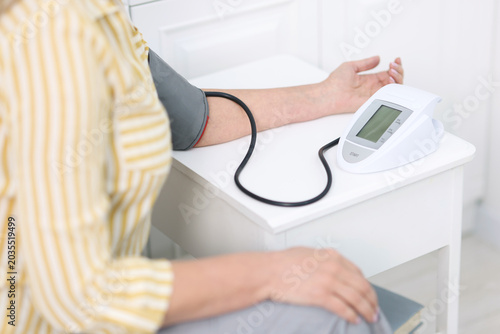 Senior woman measuring blood pressure at white table indoors, selective focus