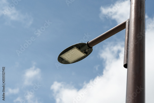 Modern LED street light on metal pole against blue sky with clouds, energy saving outdoor lighting