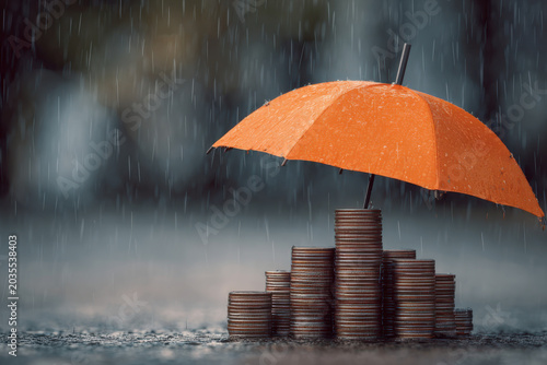 Orange umbrella protecting increasing stacks of coins from the rain