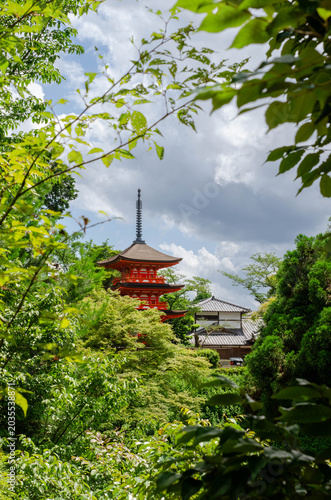Traditional Red Pagoda Framed by Green Leaves in Kyoto