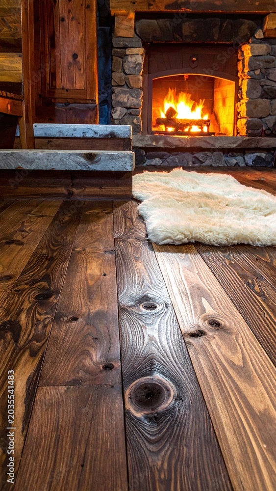 Fototapeta premium Cozy cabin interior featuring a glowing fireplace, soft sheepskin rug, and polished rustic wood floors. Perfect for winter warmth, home design, and comforting lifestyle concepts.