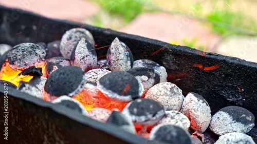 Close up of burning charcoal with flames and flying sparks in metal brazier for home barbecue or kebab cooking. Outdoor grilling scene with glowing hot coals and ash.