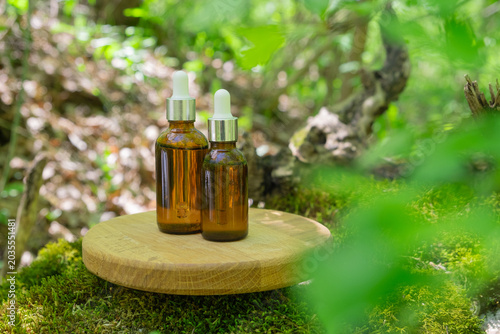 Display of brown glass bottles on wood pedestal in nature with green plants surrounding the scene