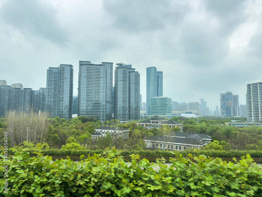 Fototapeta premium Modern Hangzhou skyline towers rising above green parkland under an overcast spring sky, China