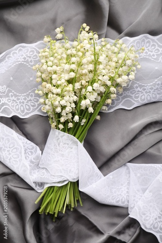 Bouquet of beautiful lily-of-the-valley flowers on grey fabric, top view