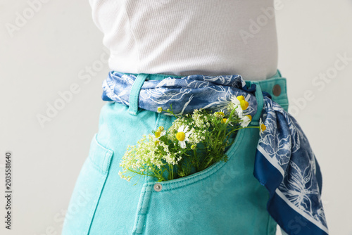 Woman with flowers in her pocket on light grey background, closeup