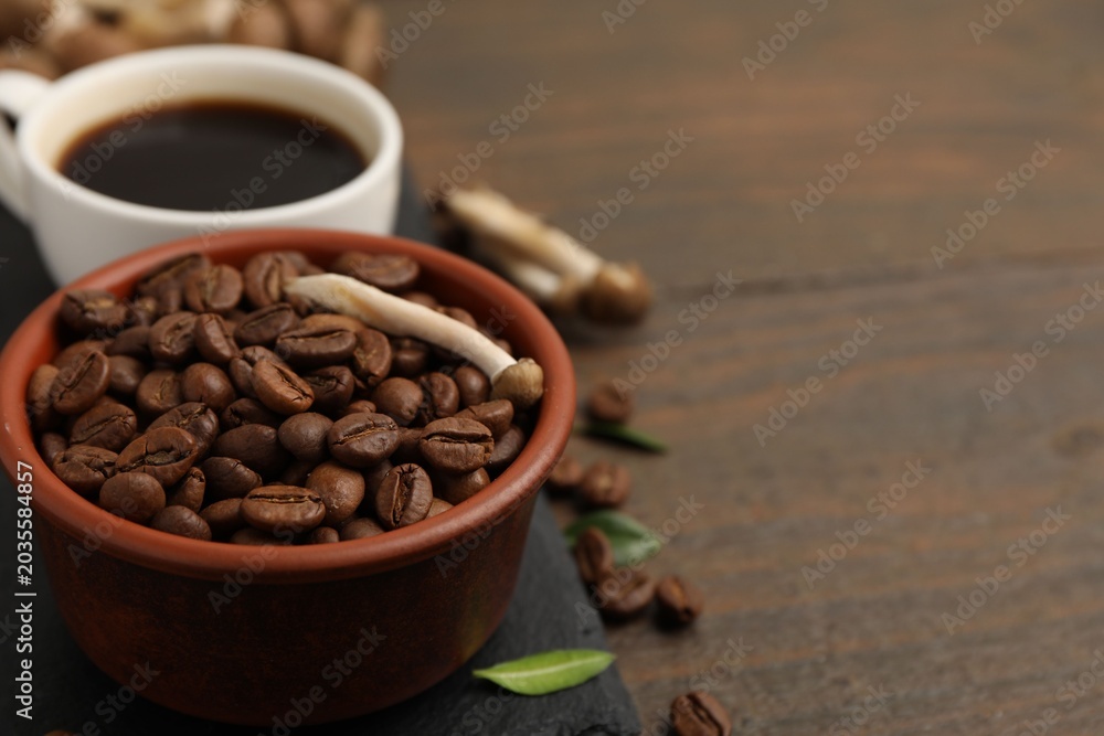 Fototapeta premium Cup of coffee, beans and mushrooms on wooden table, closeup. Space for text