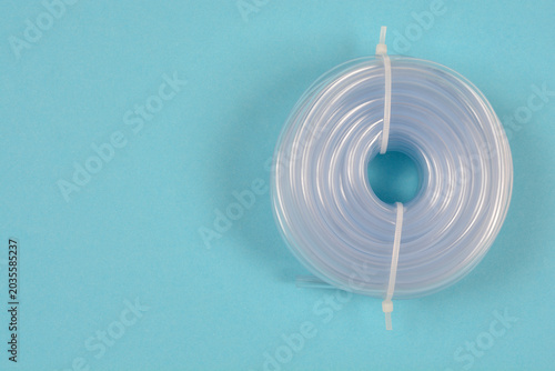 Top view of a coiled clear plastic hose secured with a zip tie placed on a solid blue background with copy space.