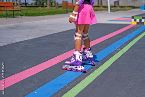 Close-up of children's roller skates. A faceless child in sports protective equipment. Vibrant urban skate Park
