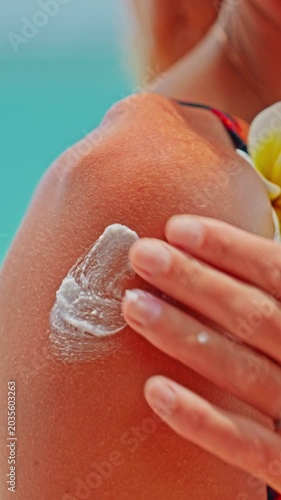 Young woman applying moisturizing sunscreen lotion on a shoulder with a beautiful ocean in the background. Skin care sun protection. Closeup
