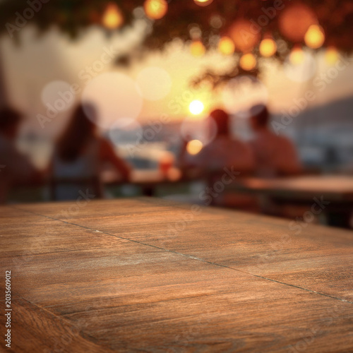 Wooden table with clean copy space for product placement and relaxing summer atmosphere with blurred summer picnic background.