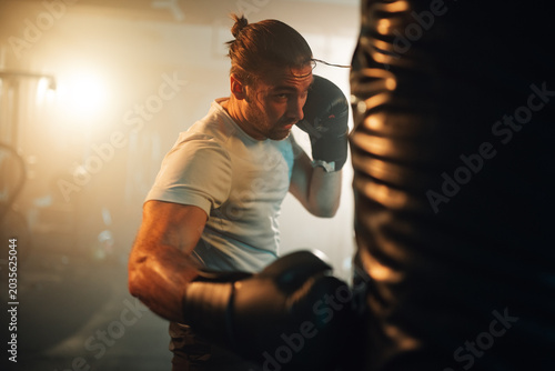 Foto Focused man exercising with boxing gloves on a heavy bag in a dimly lit fitness