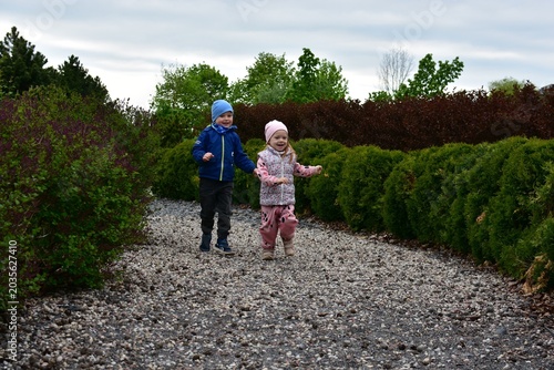 Happy little children running on gravel path between green bushes in park. Joyful childhood moment filled with friendship, outdoor play, freedom and active family lifestyle in nature.