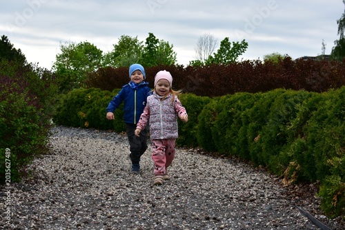 Happy little children running on gravel path between green bushes in park. Joyful childhood moment filled with friendship, outdoor play, freedom and active family lifestyle in nature.