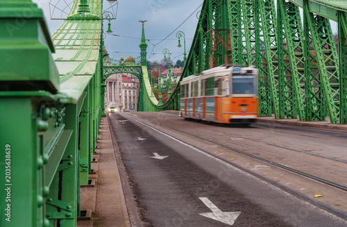 Vibrant tram traveling over a historic green metal truss bridge in Budapest A beautiful cityscape view showing urban architecture and Hungarian travel life