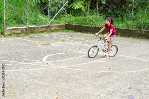 Latina girl gaining speed while riding bicycle on an outdoor concrete soccer court in park
