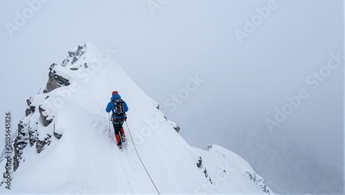 A climber ascends a snowy mountain ridge in harsh winter conditions.