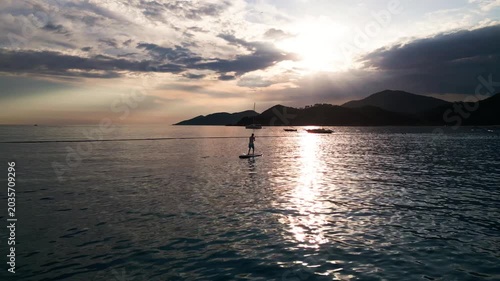 Serene sunset paddleboarding adventure with mountains and boats in the distance