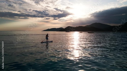 Serene sunset paddleboarding adventure with mountains and boats in the distance
