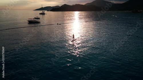 Serene sunset paddleboarding adventure with mountains and boats in the distance