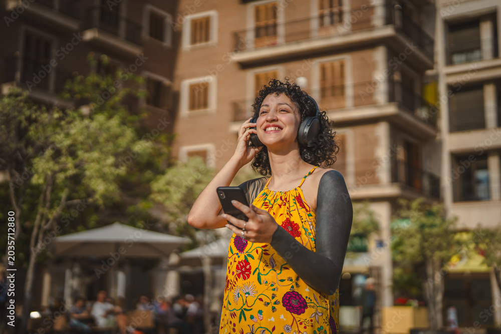 Fototapeta premium Young woman enjoying music on smart phone in city street