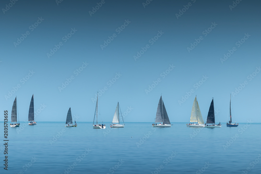 Naklejka premium Sailing yachts and sailboats aligned on a calm blue sea horizon during a regatta