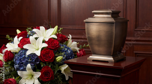 Bronze funeral urn with patriotic flower arrangement featuring lilies, roses and hydrangeas. Memorial service for American veteran after death. Respectful tribute to fallen soldier legacy.
