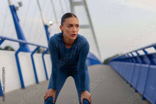 Foto Exhausted young woman in blue activewear catching her breath on bridge after run
