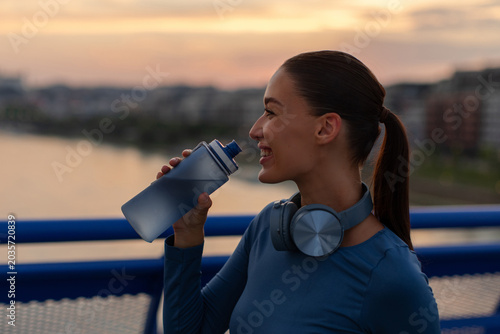 Photos Young caucasian female athlete drinking water during outdoor fitness training at
