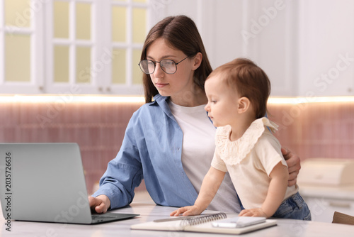 Bild auf Leinwand Young mother with her baby working in kitchen at home