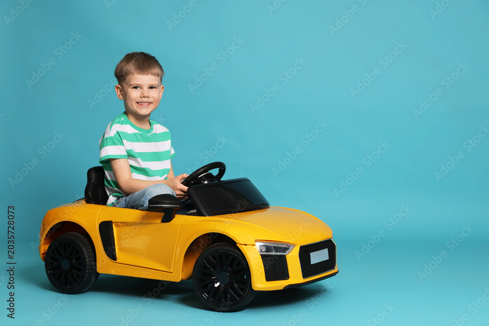 Fototapeta premium Little child driving toy car on light blue background, space for text