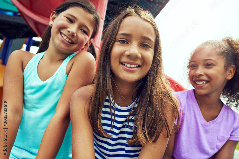 Fototapeta premium Playground, kids and girls with smile for break, summer holiday and hang out together for bonding. Group fun, portrait and childhood friends relax on weekend by jungle gym, diversity and low angle