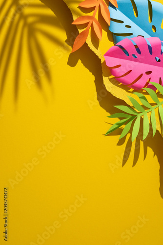 Colorful vertical paper tropical leaves on bright yellow background with summer shadows and space for text