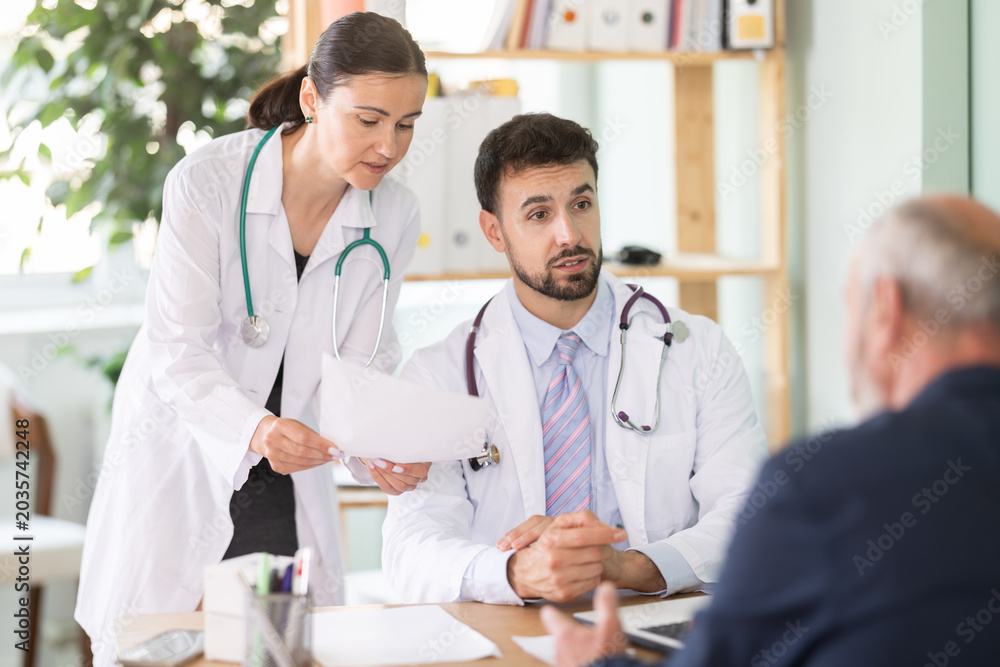 Fototapeta premium Male and female doctors are talking with a mature patient at a clinic. Discussing treatment options