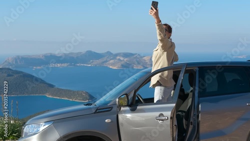 Smartphone signal loss. Young woman stops her car while driving to try to get a smartphone signal, against the backdrop of a panoramic view of the blue sea and distant islands