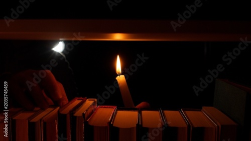 Foto Hand holding a lit candle, illuminating old books lined up on a dark shelf, symb