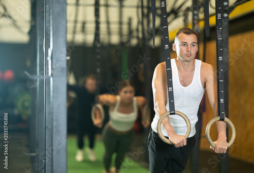 Photos Sportive young man training with gym rings in sports hall during crossfit workou