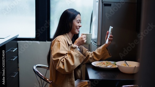 Cuadro en lienzo Young asian woman having breakfast, watching video call on smartphone, smiling