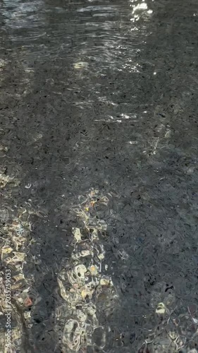 Slow motion pan of sunlight glinting on shallow riverbed water with rippling reflections in park