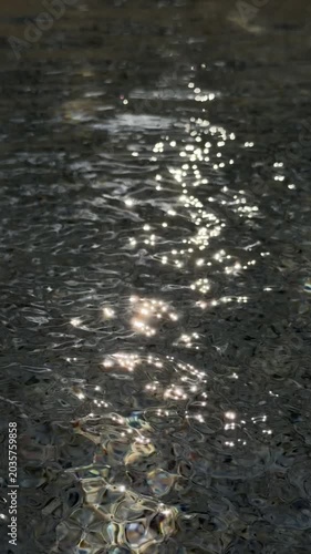 Slow motion close up of sunlight reflections shimmering on rippling water surface along shallow shoreline