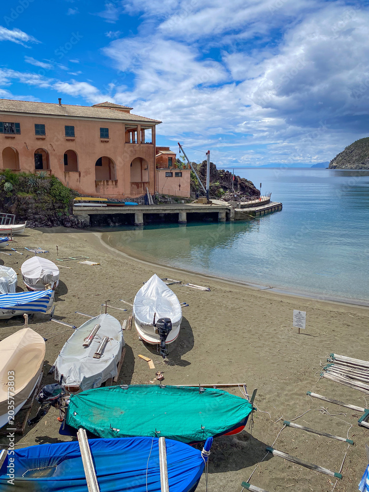 Obraz premium Small ferry terminal and pier by the sandy beach with covered boats and calm sea under dramatic clouds, in Levanto, Italy